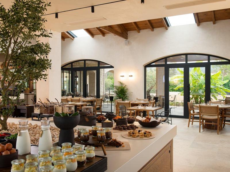 Helles Restaurant mit Buffet, Holzmöbeln und großen Fenstern, die ins Grüne blicken.