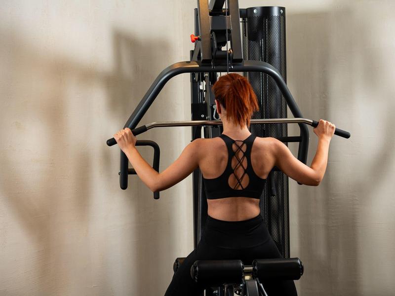 Frau trainiert Rücken auf Fitnessgerät in einem hellen Raum.