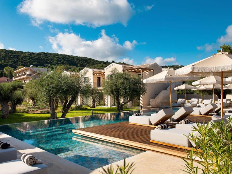 Luxuriöser Poolbereich mit Sonnenliegen und Sonnenschirmen vor einem Hotel in mediterraner Landschaft.