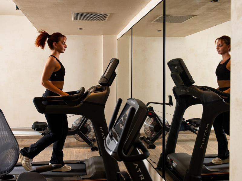 Frau trainiert auf einem Laufband in einem modernen Fitnessraum mit Spiegelwand.