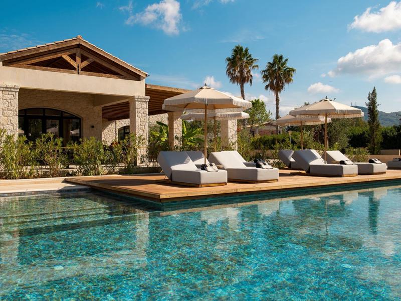 Moderner Poolbereich mit Liegen, Sonnenschirmen und mediterraner Vegetation bei Tageslicht.