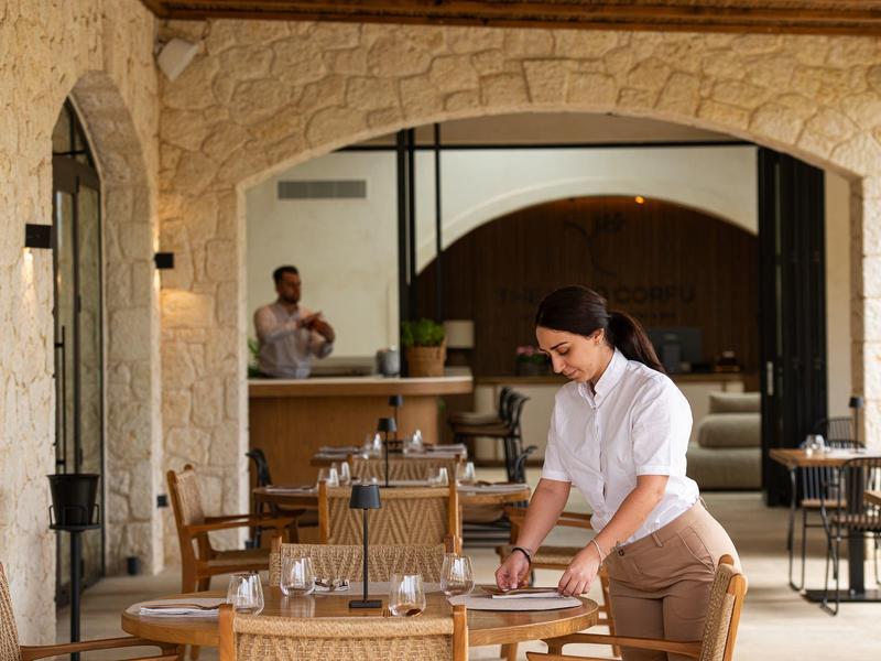 Hotelmitarbeiterin bereitet Tisch in einer stilvollen Außenbereich mit Steinmauern vor.
