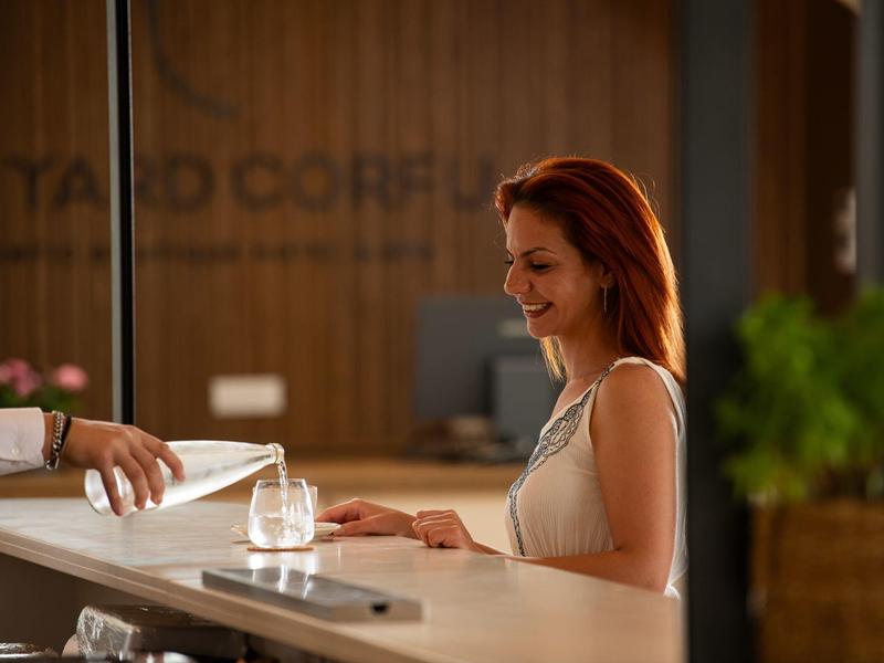 Lächelnde Frau registriert sich im Hotel an der Rezeption mit einem Glas Wasser.