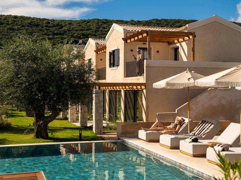 Modernes Ferienhaus mit Pool, Liegestühlen und Sonnenschirmen vor grünen Hügeln