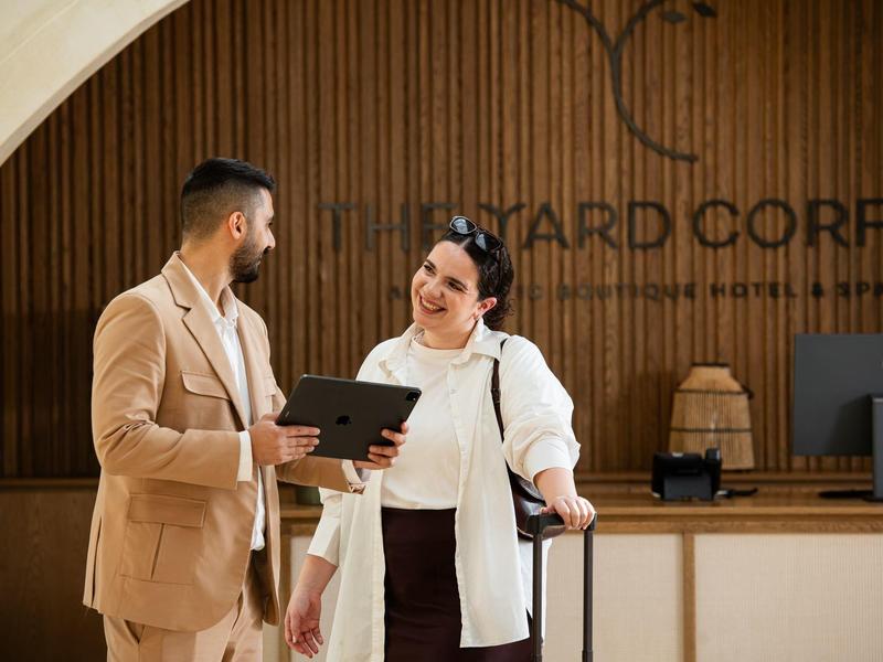 Ein Hotelgast mit Koffer spricht mit einem Mitarbeiter am Empfangstresen.