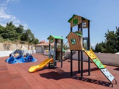 Ein bunter Spielplatz mit Rutschen und Klettergeräten auf rotem Gummiboden unter blauem Himmel.