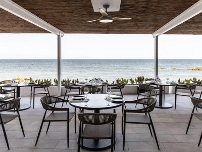 Otwarta restauracja z widokiem na morze i nowoczesnymi drewnianymi meblami pod dachem.