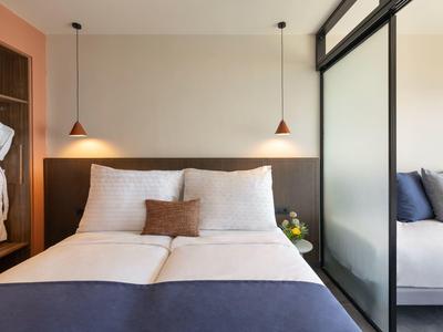 Modernes Schlafzimmer mit großem Doppelbett, zwei Leselampen und offenem Kleiderschrank.