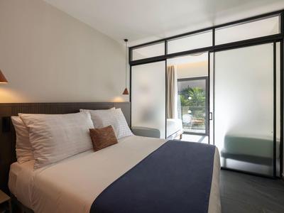 Modernes Schlafzimmer mit großem Bett, weißen Kissen, dunkler Decke und Glaswand zum Balkon.