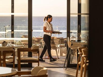 Kelnerka niesie tace przez nowoczesną restaurację z widokiem na morze.