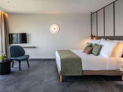 Modernes Schlafzimmer mit großem Bett, grünen Akzenten, einem Stuhl und einem Fenster mit Vorhängen.