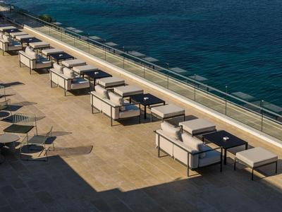 Kilka białych sof lounge z stolikami wzdłuż tarasu z widokiem na morze.