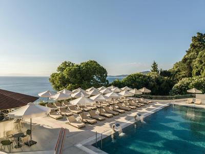 Basen hotelowy z leżakami i parasolami z widokiem na morze pod czystym niebem.