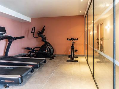 Nowoczesna siłownia z bieżniami, orbitrekami i rowerem stacjonarnym obok szklanych drzwi.