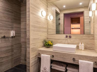 Modernes Badezimmer mit hellen Marmorfliesen, großem Spiegel, Waschbecken und Dusche links.