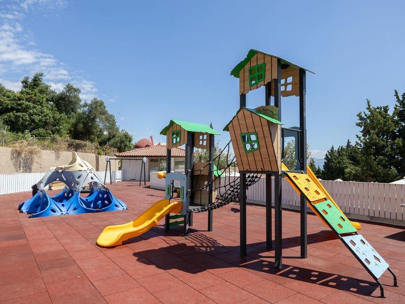 Ein bunter Spielplatz mit Rutschen und Klettergeräten auf rotem Gummiboden unter blauem Himmel.