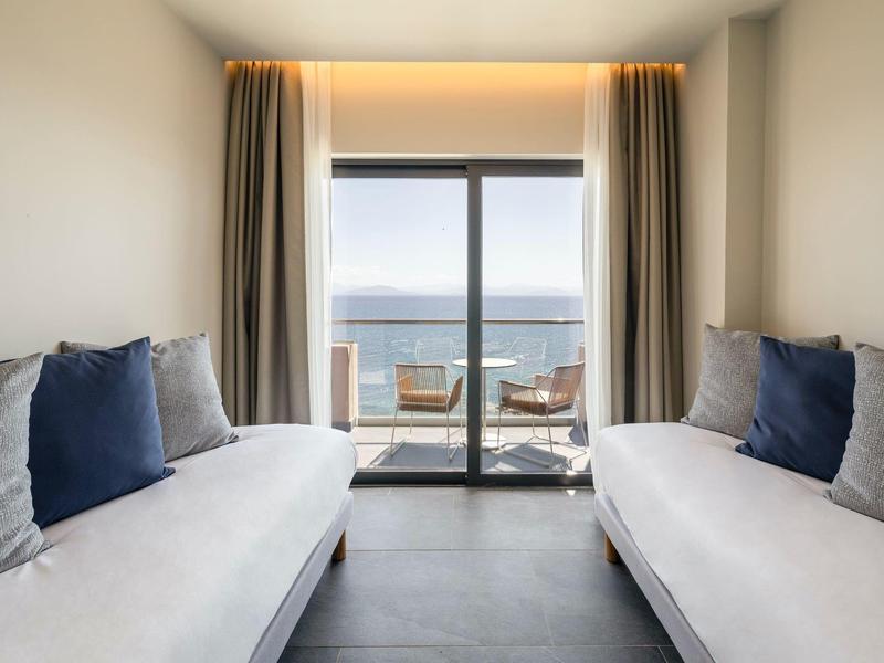 Modernes Zimmer mit zwei weißen Sofas, blauen Kissen und Zugang zu Balkon mit Meerblick.