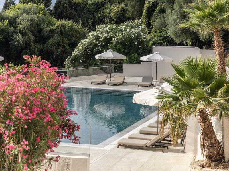 Ein ruhiger Poolbereich mit Liegen, Schirmen und blühender Vegetation in sonniger Umgebung.
