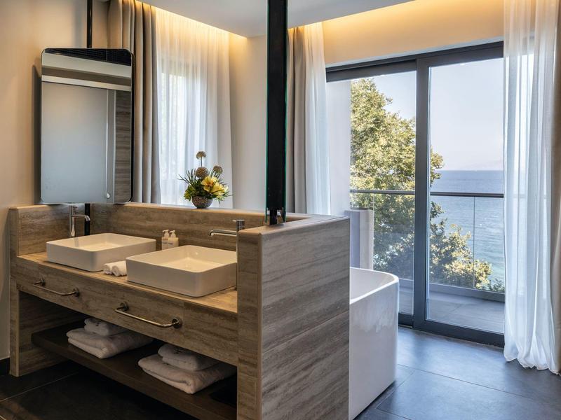 Moderner Badezimmerspiegel mit Doppelwaschbecken, Holzverkleidung und Balkonblick auf Natur und Meer.