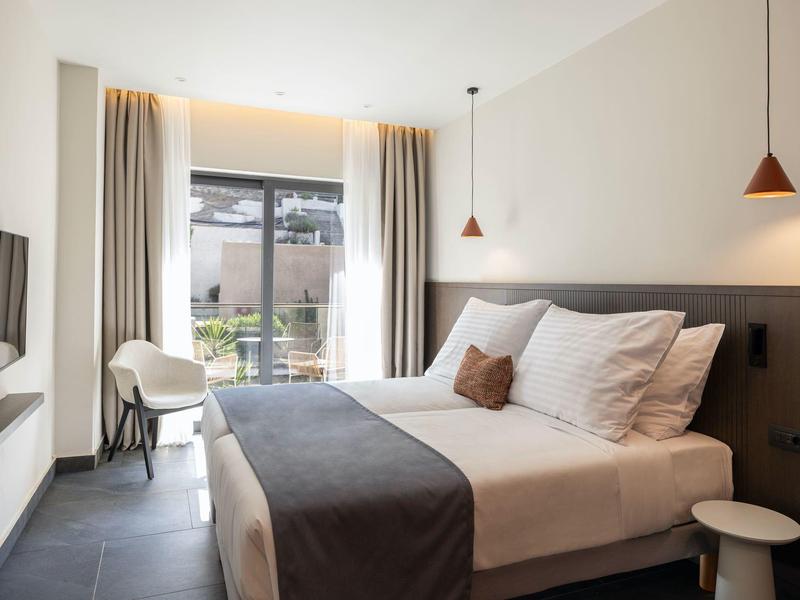 Modernes Schlafzimmer mit großem Bett, weißen Wänden, grauem Bettläufer und Terrasse draußen.