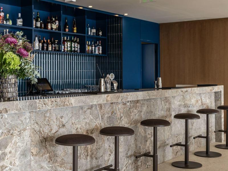 Moderner Barbereich mit Holzstühlen, weißgrauer Steinbar und blau gestrichener Wand im Hintergrund.