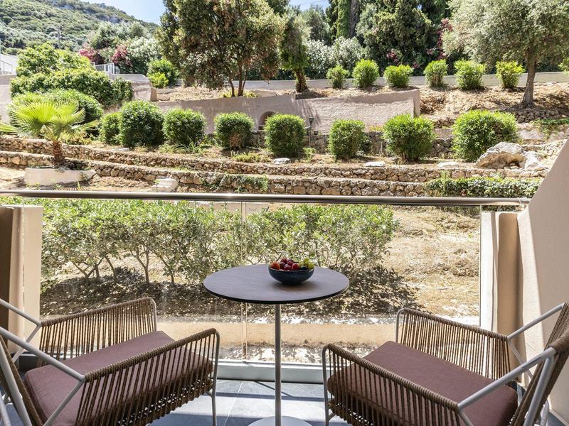 Balkon mit zwei Stühlen und einem kleinen Tisch, Blick auf Garten mit Büschen und Bäumen.
