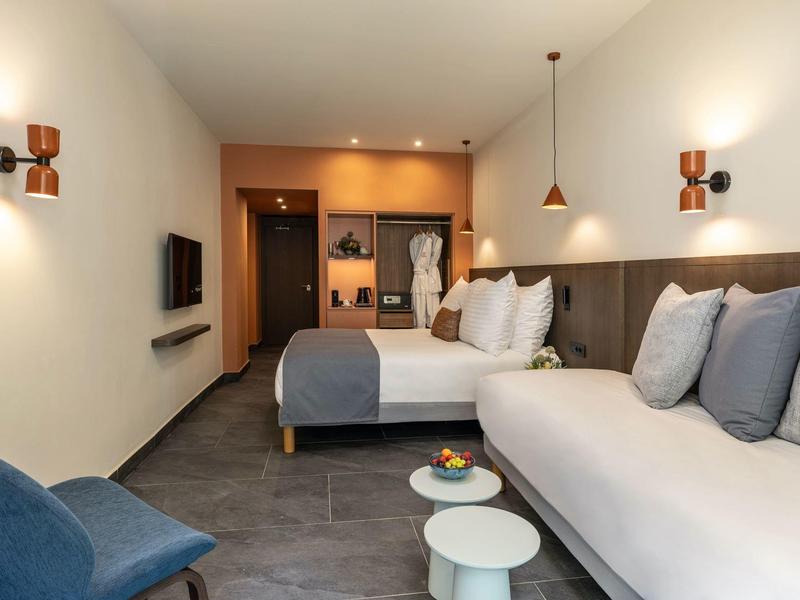 Modernes Hotelzimmer mit Bett, Sofa, Sesseln und integriertem Kleiderschrank in warmem Licht.