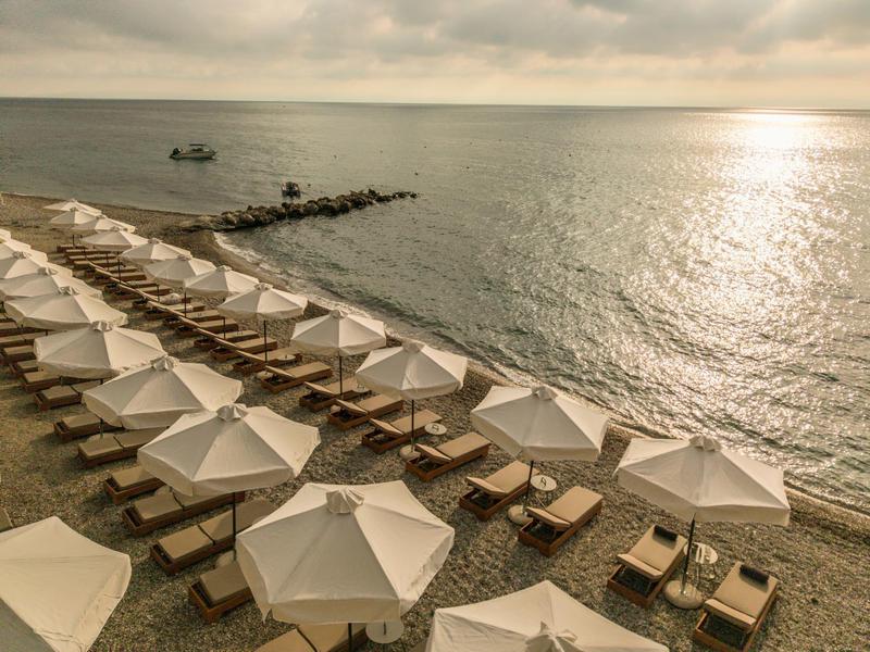 Strand mit Reihen weißer Sonnenschirme und Liegestühle vor ruhigem Meer und bewölktem Himmel.