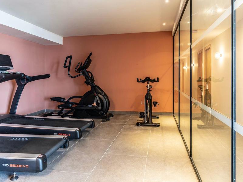 Moderner Fitnessraum mit Laufbändern, Crosstrainern, Spinningrad und gläserner Trennwand.