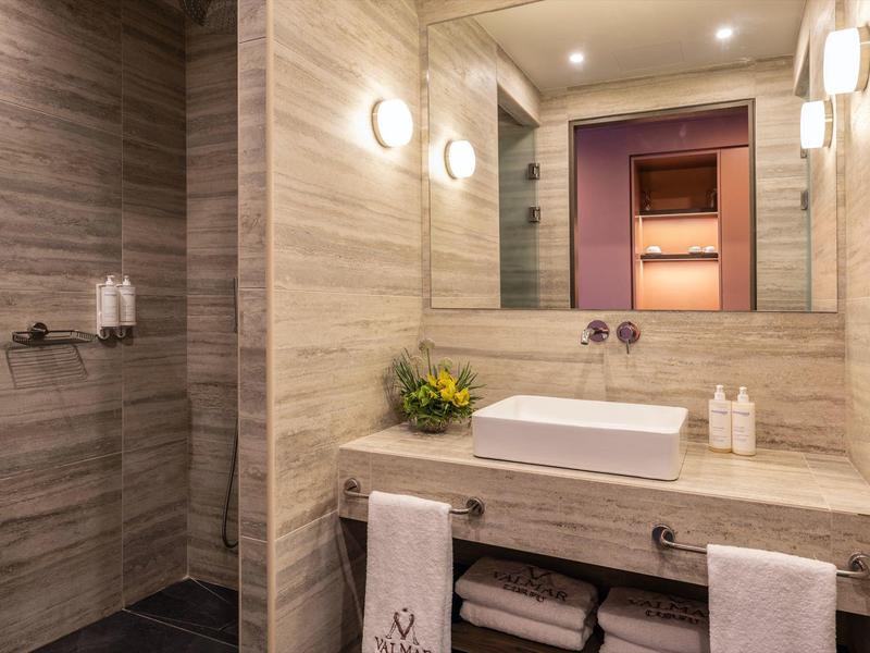 Modernes Badezimmer mit hellen Marmorfliesen, großem Spiegel, Waschbecken und Dusche links.