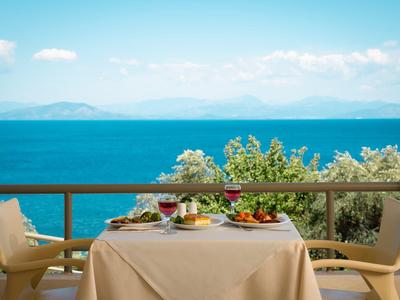 Ein gedeckter Tisch mit Wein und Salat auf einer Terrasse mit Blick auf das blaue Meer und Himmel.
