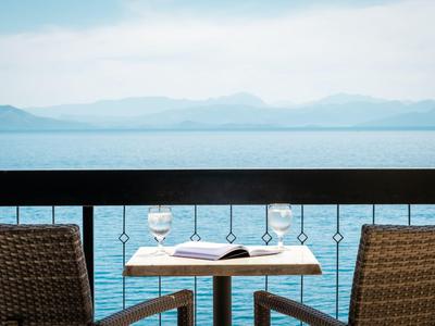 Terraza con mesa, dos sillas, libro abierto y vaso frente a lago y montañas.