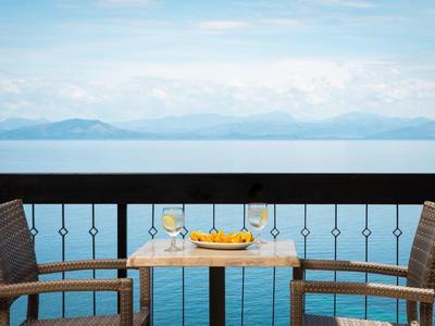 Zwei Stühle und ein Tisch mit Orangenschale auf Balkon mit Blick auf ruhiges Meer und Berge.