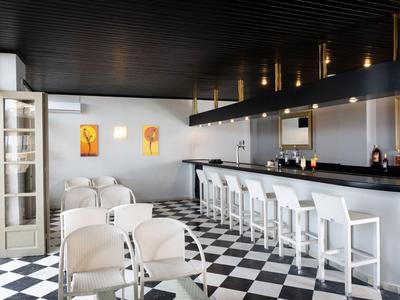 Área de bar de hotel moderna con mostrador blanco, taburetes y suelo ajedrezado en blanco y negro.