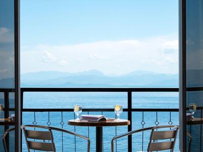 Balkontisch mit zwei Stühlen, Kerzen und Buch, Blick auf ruhiges Meer und Berge im Hintergrund.