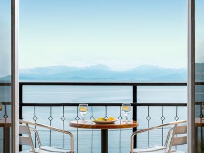 Balkontisch mit Getränken, Blick auf Meer und Berge bei klarem Himmel.
