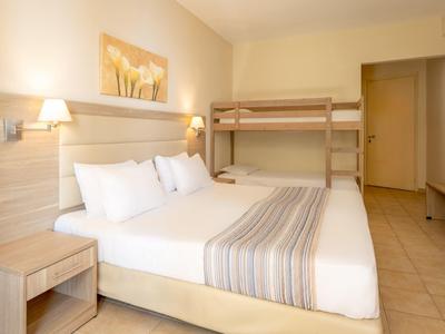 Helles Schlafzimmer mit Doppelbett, Etagenbett, Nachttischen und Wandlampen.