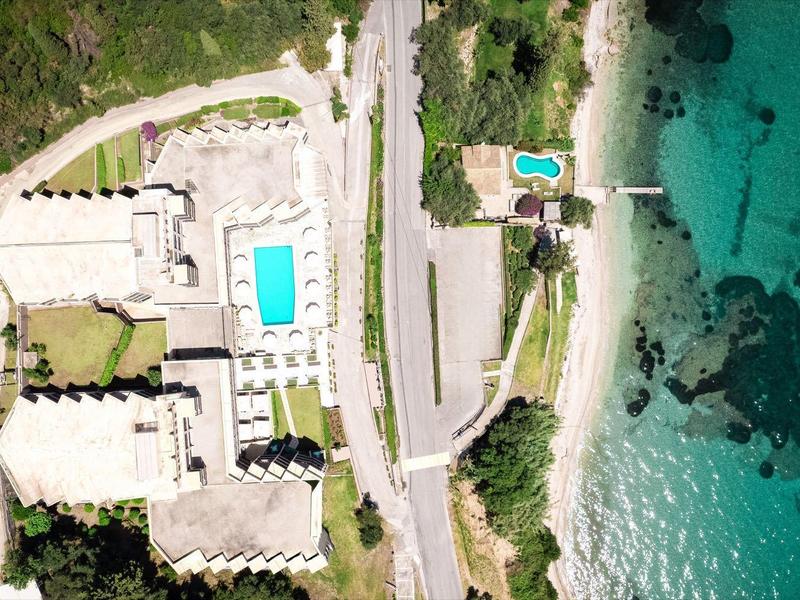 Luftaufnahme eines Hotels mit Pool neben Straße und kristallklarem türkisfarbenem Meer.