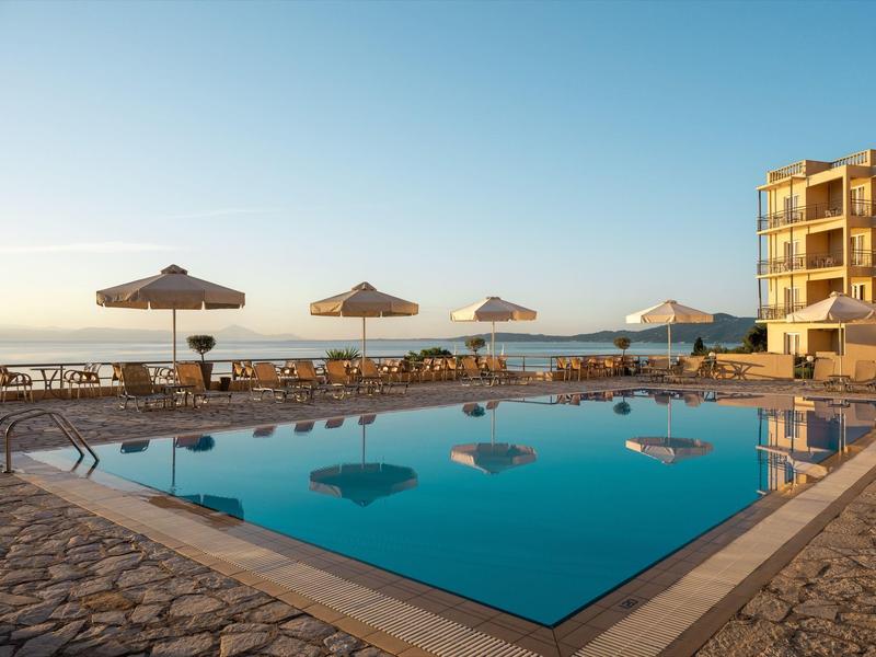 Großer rechteckiger Pool mit Sonnenschirmen, Liegestühlen und einem mehrstöckigen Gebäude im Hintergrund.