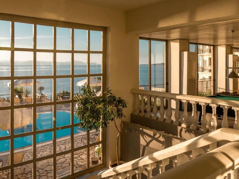 Wohnzimmer mit großem Fenster, Meerblick, Pool draußen und Sonnenlicht, das den Raum wärmt.