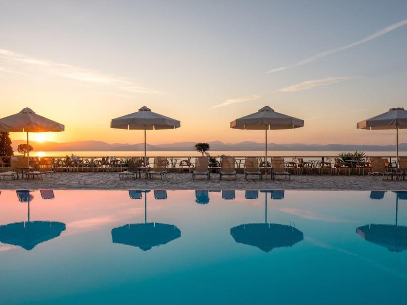 Pool mit ruhigem Wasser, vier Sonnenschirmen und Sitzgelegenheiten am Sonnenuntergang am Meer.