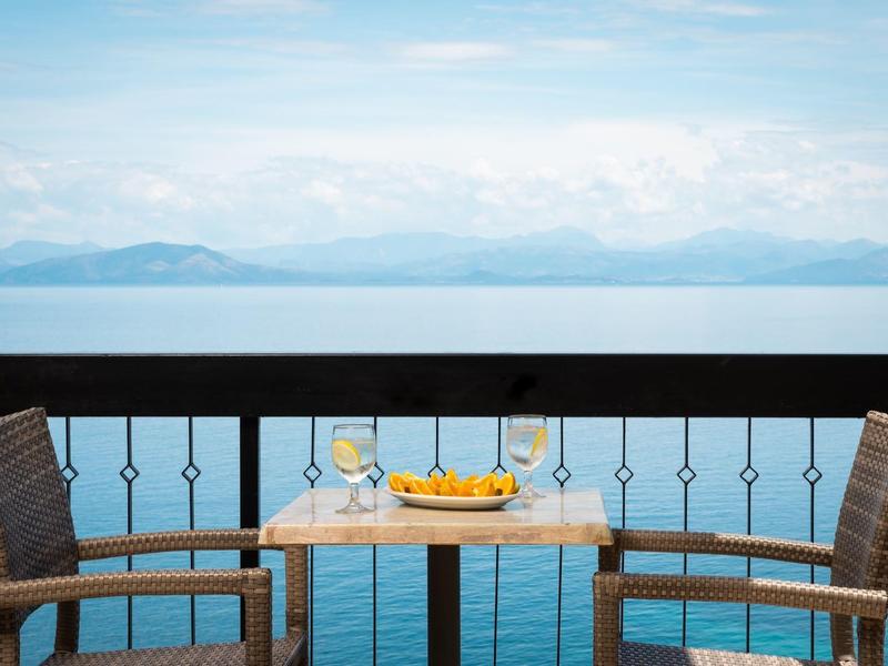 Zwei Stühle und ein Tisch mit Orangenschale auf Balkon mit Blick auf ruhiges Meer und Berge.