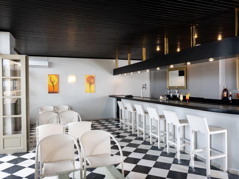 Moderner Barraum mit schwarz-weißem Schachbrettboden, weißen Stühlen und dunklem Holzdecke.