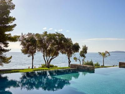 Piscina a sfioro con vista sul mare e alberi sotto un cielo limpido.