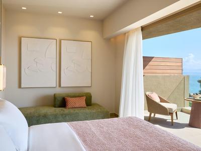 Modernes Hotelzimmer mit gemütlichem Bett und Sitzbereich mit Blick auf Balkon und Meer.