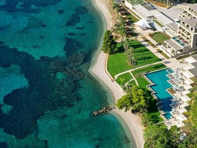 Luftaufnahme eines Resorts mit Pools an einem klaren Strand und türkisfarbenem Meer.