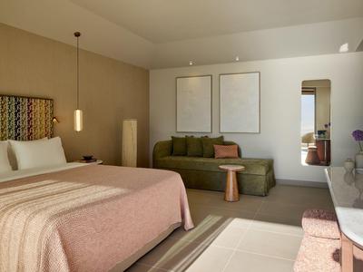 Helles Hotelzimmer mit großem Bett, grünem Sofa, Holztisch und minimalistischer Dekoration.