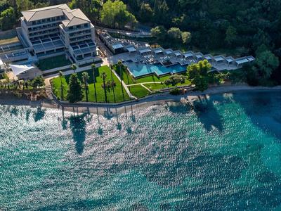 Luxushotel mit Pool und direktem Zugang zu einem klaren, blauen Meer, umgeben von grünen Bäumen.