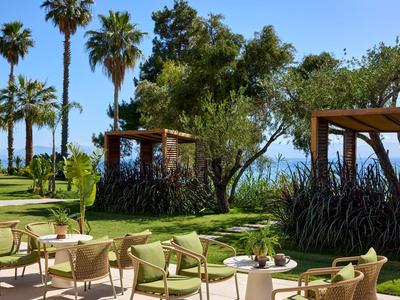 Outdoor-Lounge mit bequemen Stühlen, Tischen und grüner Umgebung bei klarem Himmel am Meer.