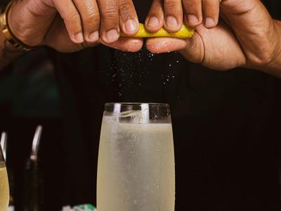 Mani che spremono una fetta di limone sopra un bicchiere di bevanda frizzante.